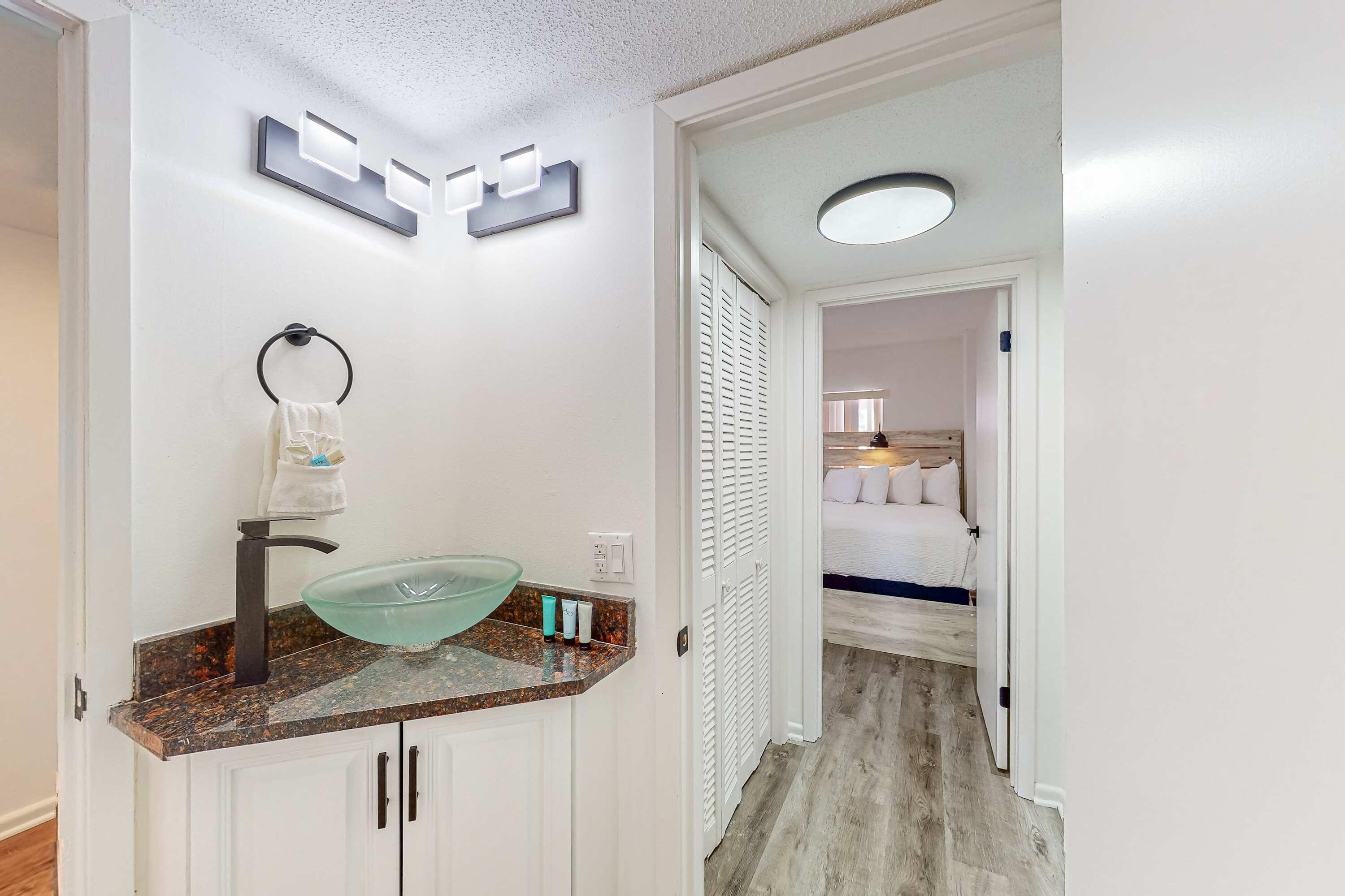 A bathroom with a glass bowl sink, white cabinets, and a towel ring.