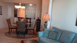 Ein Wohnzimmer mit einem hellblauen Sofa, einem schwarzen Hocker und einem Essbereich mit Tisch und Stühlen.