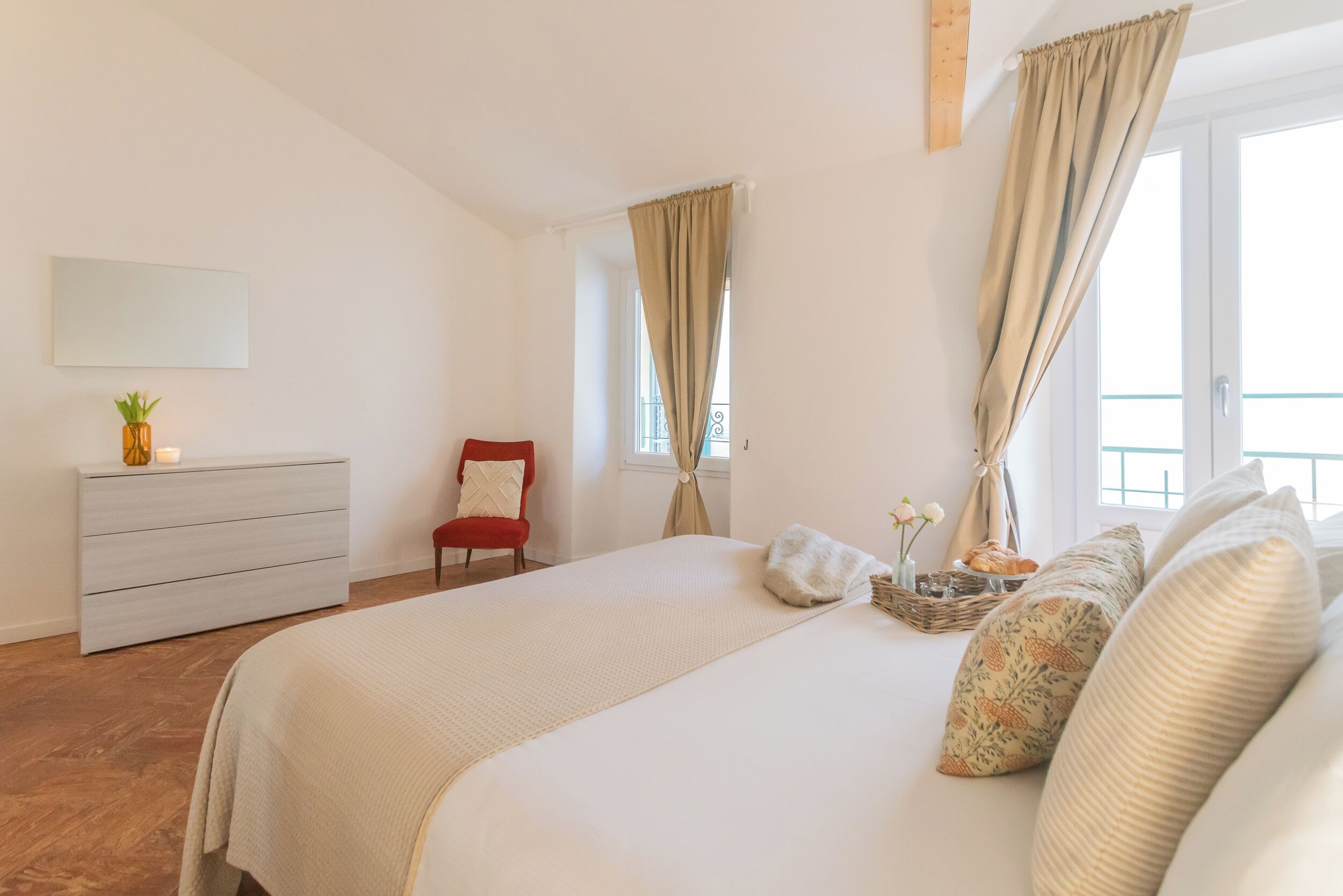 Une chambre à coucher avec un grand lit, une commode, une chaise et une fenêtre avec des rideaux.