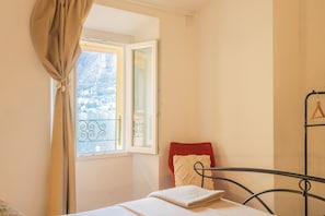 A room with a bed, a window with curtains, a view of a balcony, and a metal bed frame.