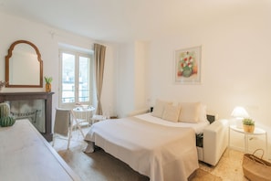 A hotel room with a bed, a desk, a chair, a small table, and a window with curtains.