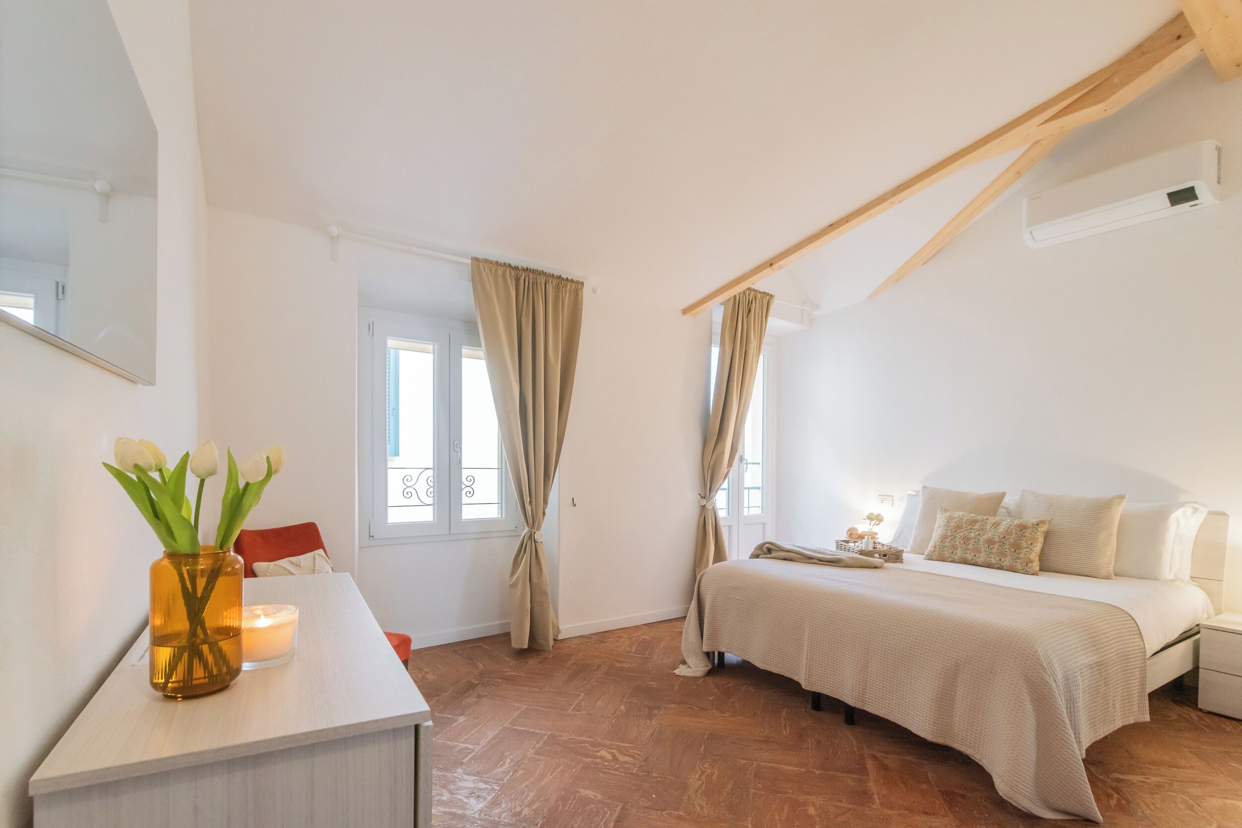 A bedroom with a bed, bedside table, and a vase with flowers.
