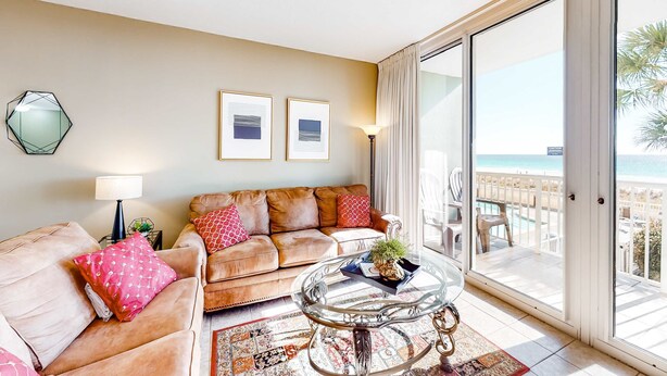 Una sala de estar con sofá, sillones, una mesa de centro de vidrio y vista a la playa a través de amplios ventanales correderas.