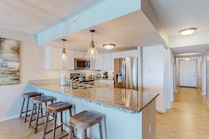 A modern kitchen with granite countertops, stainless steel appliances, and bar stools. - Playing Hooky, Islander E 7012 - Elegant oceanfront condo with pool & gym access (Fort Walton Beach)