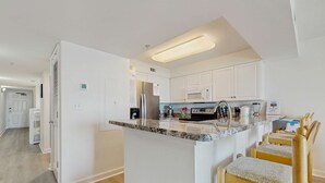 Uma cozinha moderna com armários brancos, bancada de granito e uma ilha planejada com banquetas.