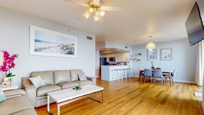 A spacious living room with a sofa, coffee table, and a dining area with chairs and a table. - Beautiful beachfront home with shared pool and beach access (Fort Walton Beach)
