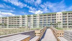 A wooden boardwalk leading to a multi-story building with balconies, overlooking a beach. - Beautiful beachfront home with shared pool and beach access (Fort Walton Beach)
