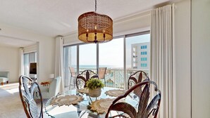 Een moderne eethoek met een glazen tafel, rieten stoelen en een hanglamp.