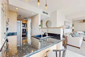 A modern kitchen with a granite countertop, stainless steel sink, and overhead lighting. - Stunning oceanfront condo with access to a shared pool and private beach entry (Fort Walton Beach)