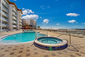 A hotel pool area with a hot tub, lounge chairs, and a view of the beach. - Beachfront condo with beach chairs, an umbrella, and a pool (Fort Walton Beach)