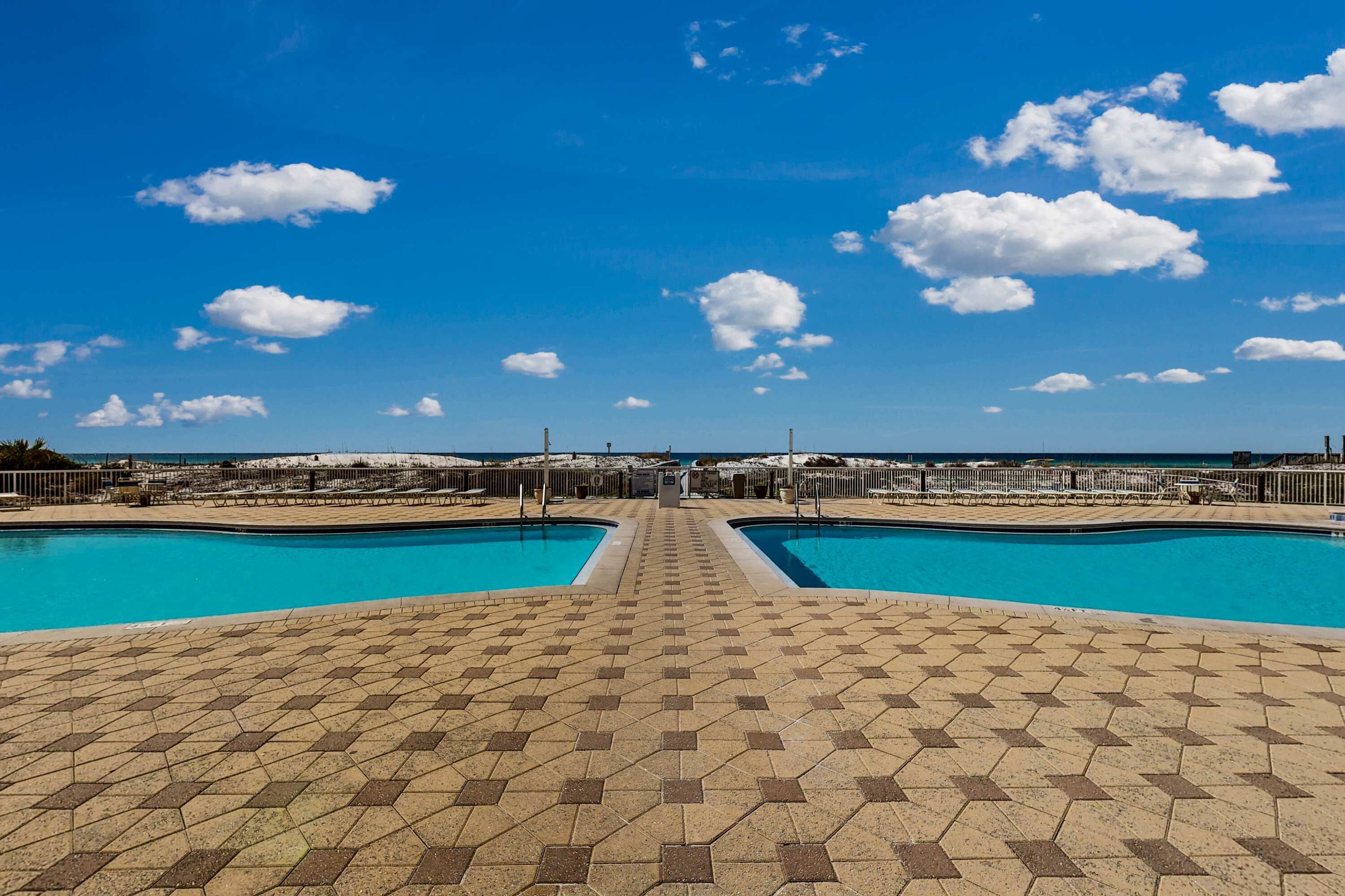Une piscine avec une allée dallée qui mène à un point de vue éloigné sur une zone côtière.