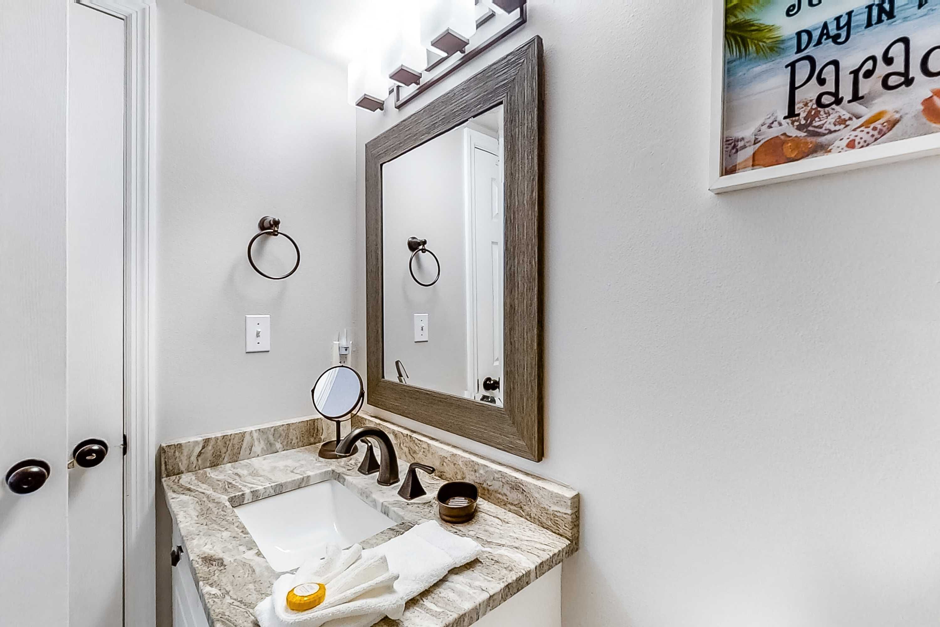 Un baño con encimera de mármol, lavabo, espejo y barra para toallas.