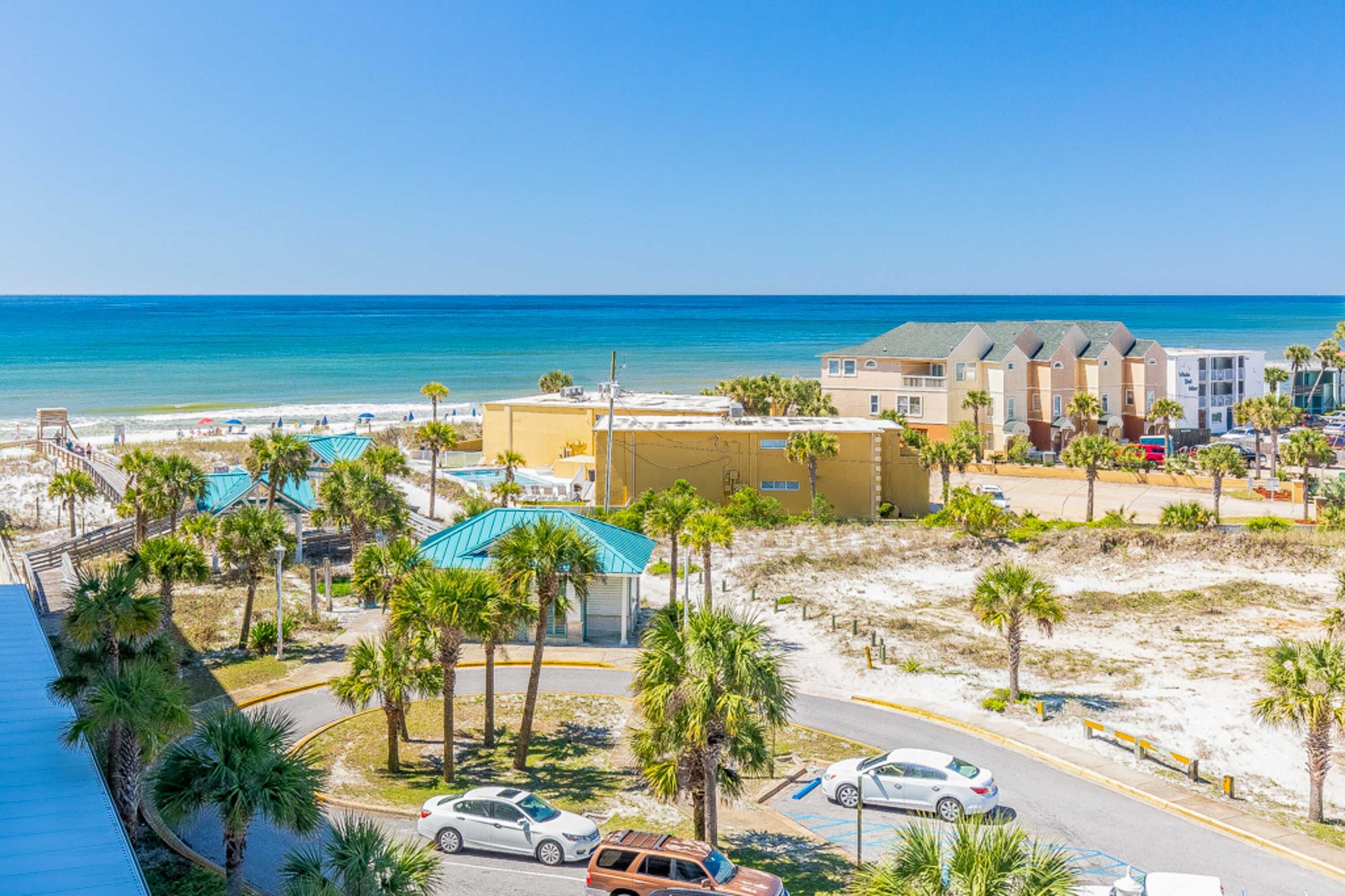 Un hotel frente al mar con vistas a la playa, varias edificaciones y coches aparcados.