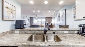 Een moderne keuken met een dubbele spoelbak, granieten aanrechtbladen en verlichting boven het aanrecht.