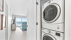 Una lavanderia con due lavatrici affiancate, una porta che dà su un balcone e un piccolo armadietto bianco.