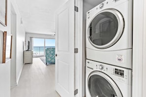 A laundry room with two stacked front-loading washing machines, a door leading to a balcony, and a small white cabinet. - Second-Floor Gulf-front Condo with Beach Service & pool (Miramar Beach)