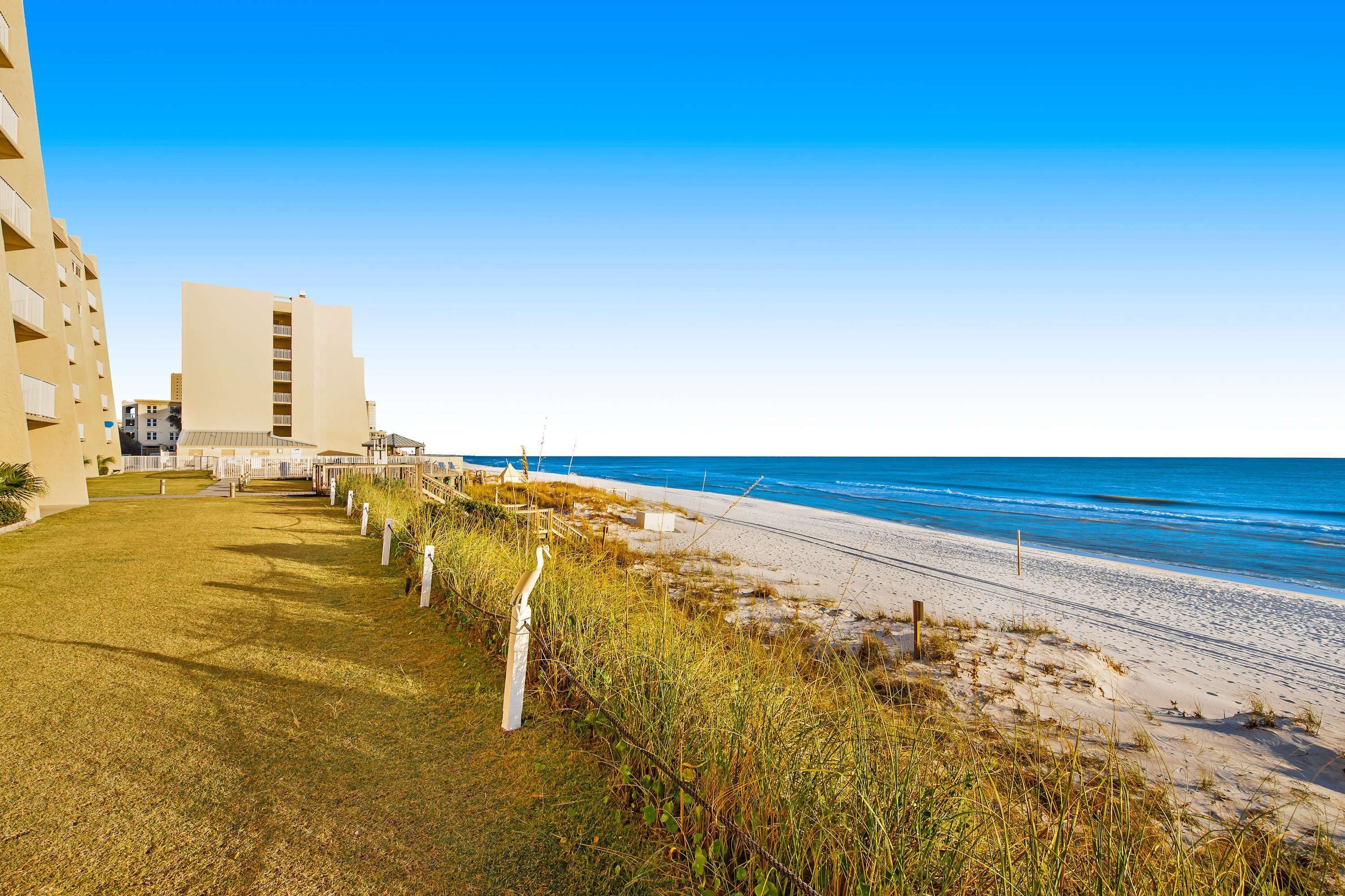 A beachfront hotel with a grassy lawn, a pathway leading to the beach, and a view of the ocean.