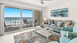 Un soggiorno con balcone vista spiaggia, una ventola a soffitto, un divano e un tavolino da caffè.