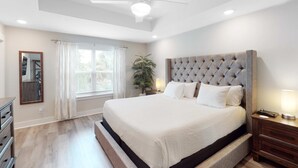 A bedroom with a large bed, a ceiling fan, a nightstand with a lamp, and a window with curtains. - Stylish, dog-friendly townhome with firepit & enclosed yard - blocks to downtown (Pensacola)