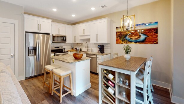 A modern kitchen with white cabinetry, stainless steel appliances, and a wooden dining table. - Stylish, dog-friendly townhome with firepit & enclosed yard - blocks to downtown (Pensacola)