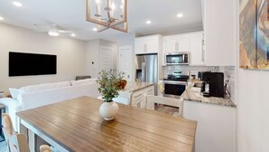 A modern kitchen with white cabinets, stainless steel appliances, and a wooden dining table. - Stylish, dog-friendly townhome with firepit & enclosed yard - blocks to downtown (Pensacola)