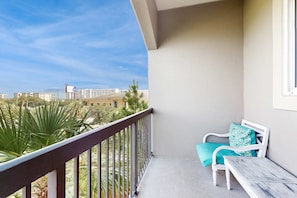 A balcony with a white chair and table, a view of buildings and greenery, and a clear sky. - Beautiful Third-floor Condo with Private Balcony, Shared Pool & Hot Tub, Central AC (Miramar Beach)