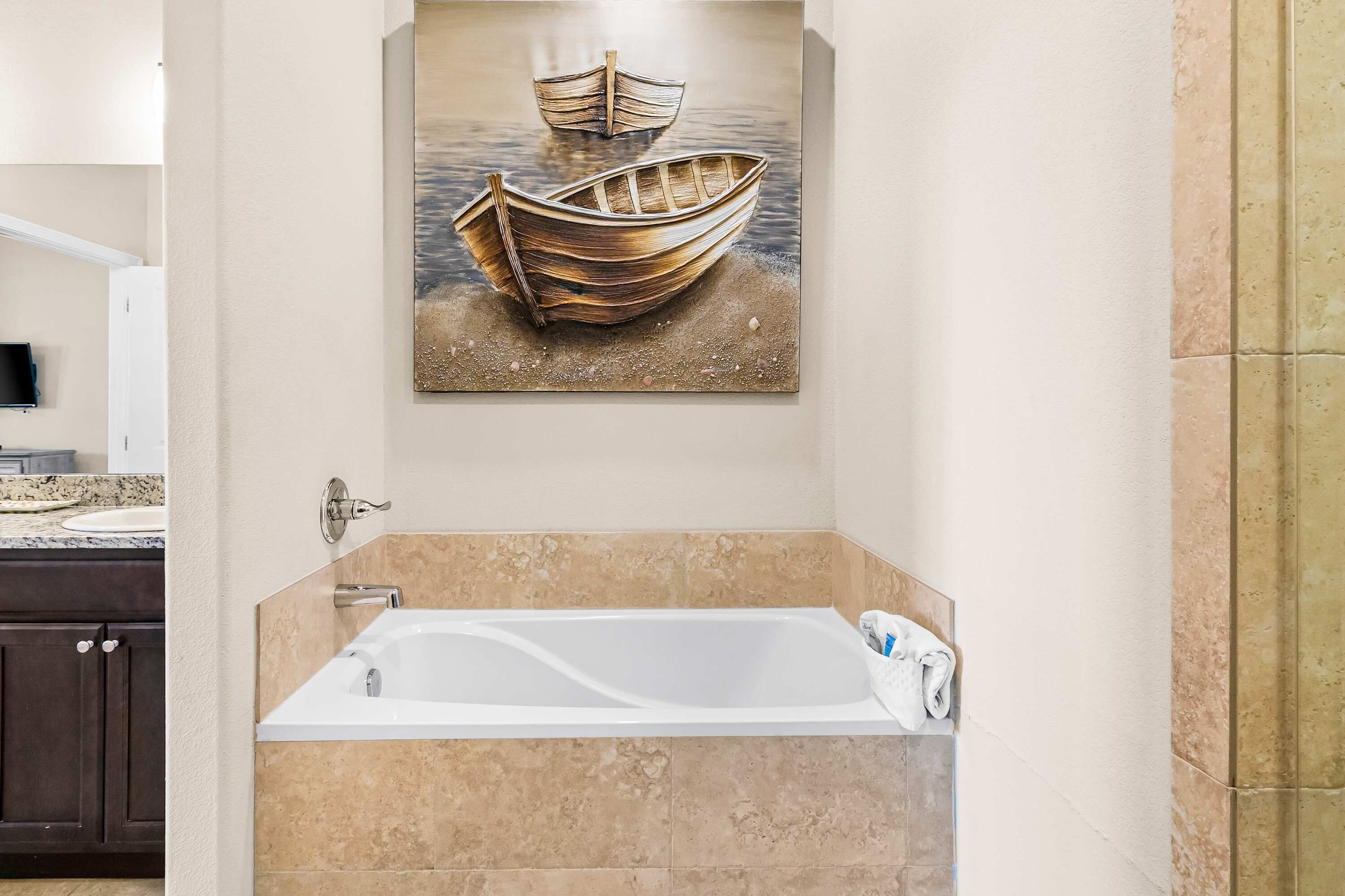 A bathroom with a bathtub, a painting of a boat on water, and a granite countertop.