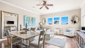Amplia sala de estar con comedor, ventilador de techo y ventanas grandes que ofrecen vistas al exterior.