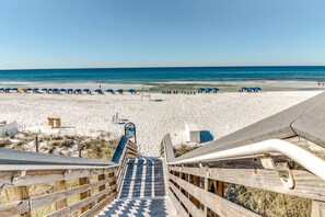 Eine Holztreppe führt zu einem Strand mit weißem Sand und blauem Himmel.