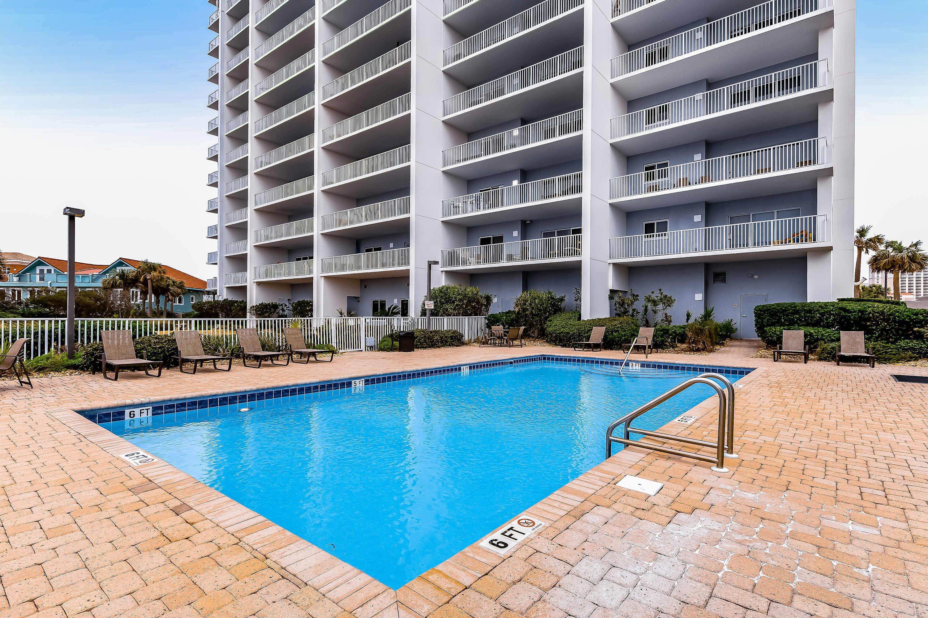 Une piscine dont la profondeur maximale est indiquée à 6 pieds, entourée d’une terrasse en briques et bordée de rampes blanches.