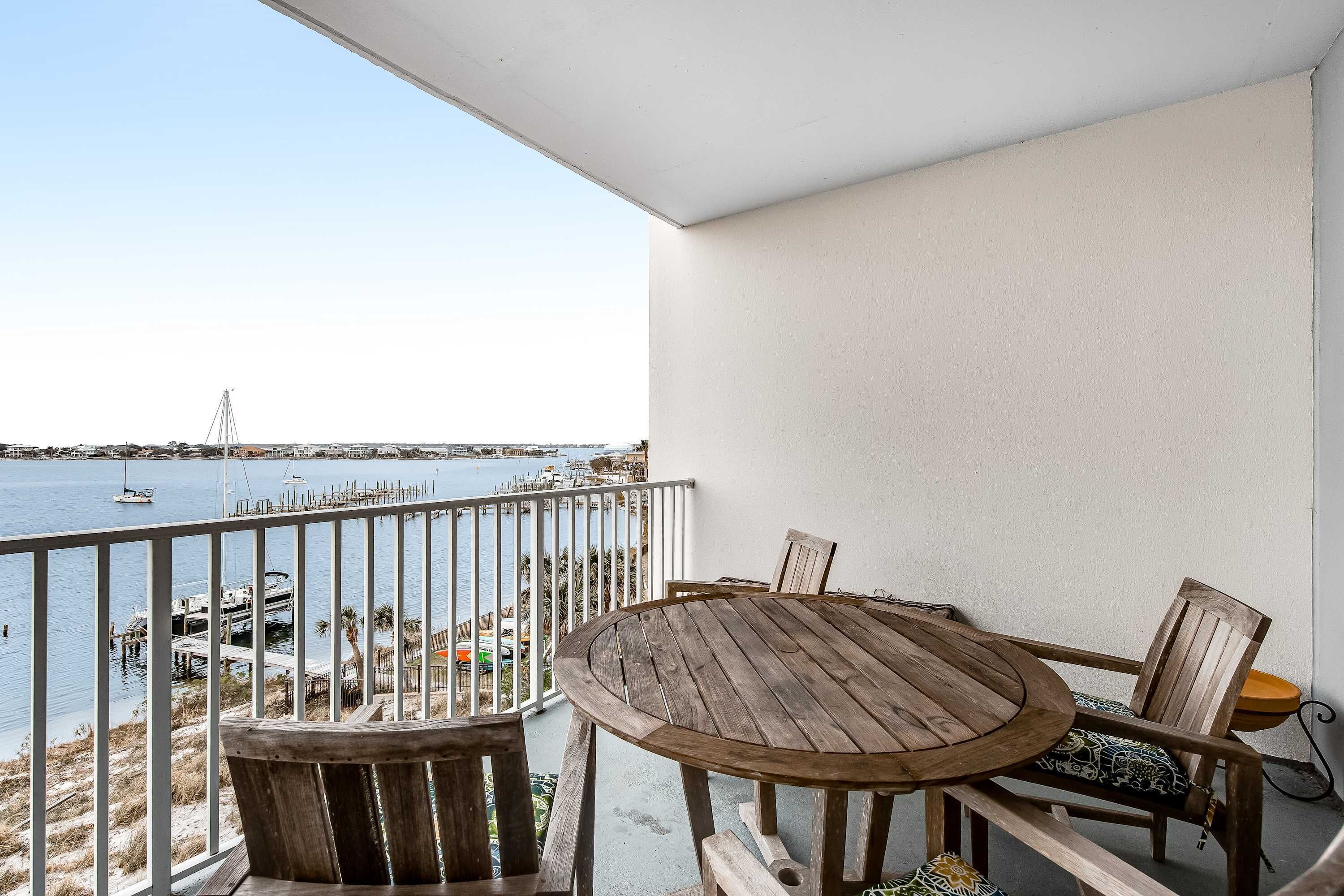 Una mesa y sillas de madera en un balcón con vista al agua y barcos.