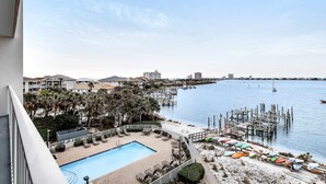 A pool area with lounge chairs and a view of the beach and water. - 4th Floor Bayfront Condo With Private W/D & Shared Outdoor Pool (Pensacola Beach)