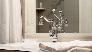 Une salle de bain avec un robinet chromé, un lavabo blanc et un miroir qui reflète l’ensemble de la pièce.