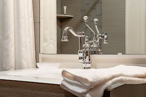 Ein Badezimmer mit einem chromfarbenen Wasserhahn, einem weißen Waschbecken und einem Spiegel, der das Badezimmer widerspiegelt.