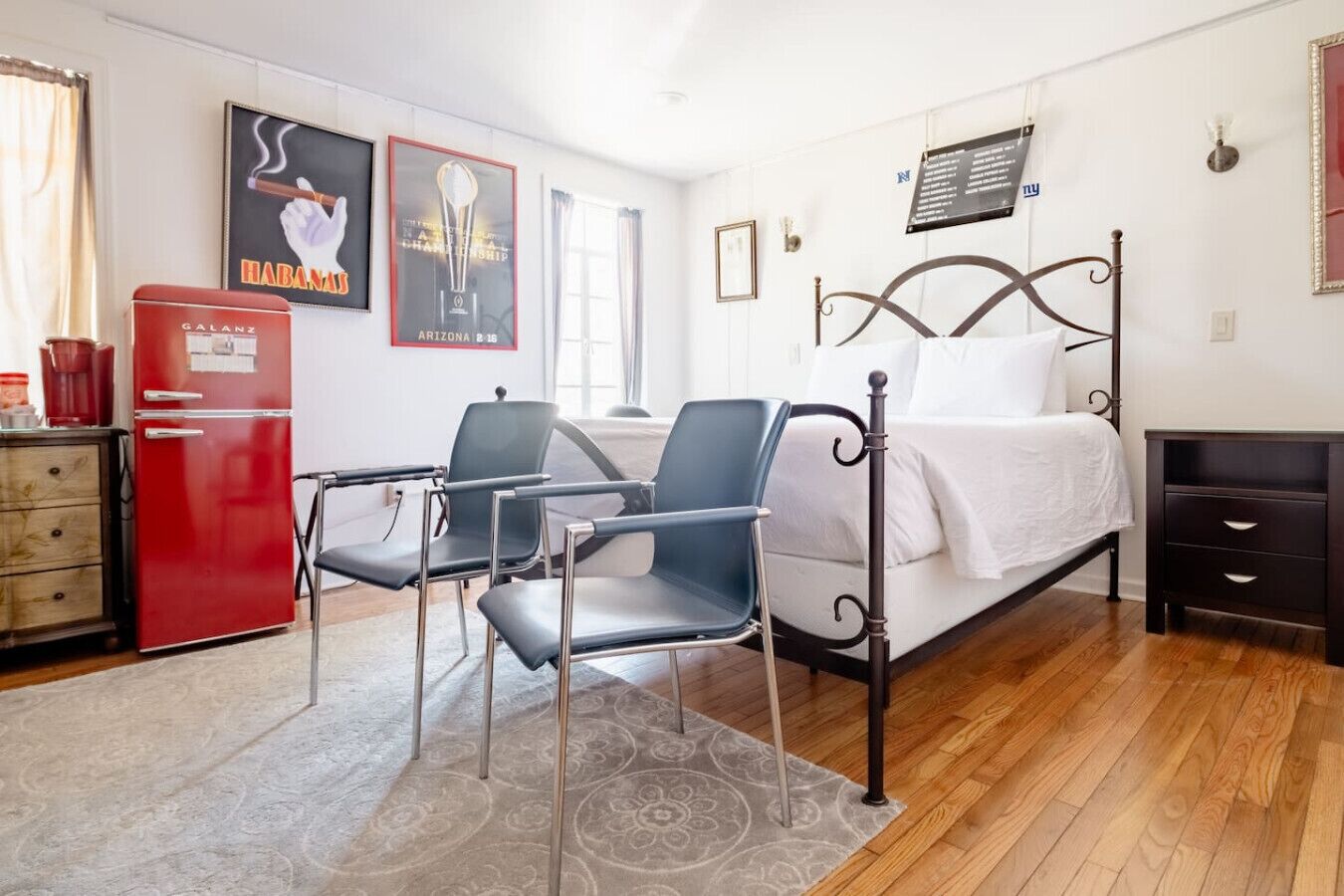 Een slaapkamer met een bed, een bureau, een stoel, een rode koelkast en een muur met posters.
