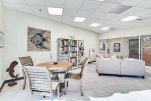 Ein helles Zimmer mit einem Holzesstisch, Stühlen, einem Bücherregal und einem Sofa.