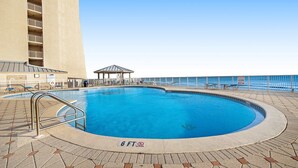 A swimming pool with a 6 FT depth limit, surrounded by a tiled deck and a building with balconies. - Fifth-floor, oceanfront condo with fast WiFi & pool  -  snowbirds OK (Miramar Beach)