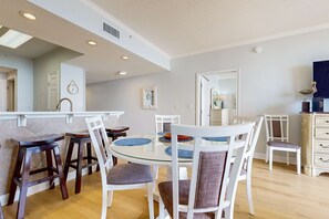 Un espace repas avec une table ronde en verre, des chaises blanches et des tabourets en bois.