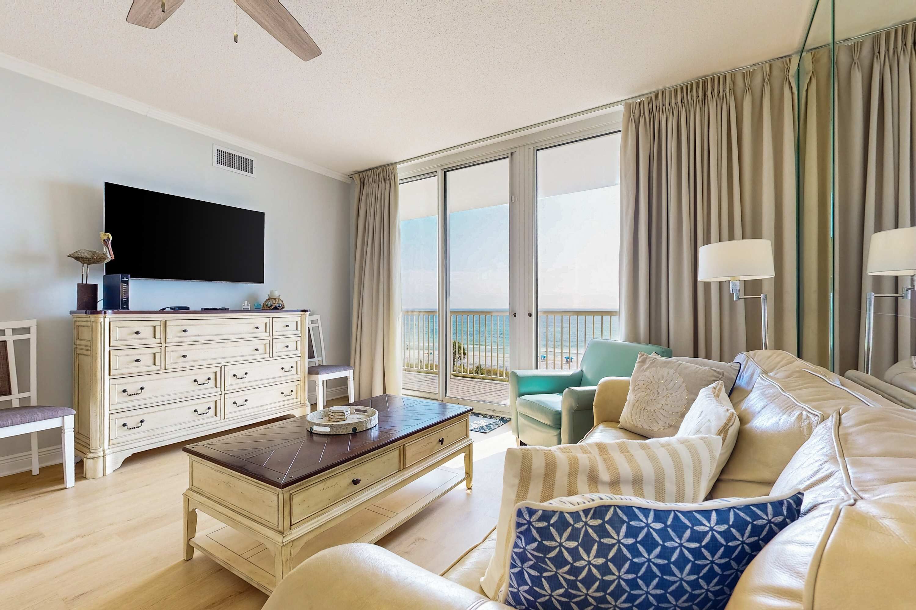 Ein geräumiges Wohnzimmer mit einem großen Flachbildfernseher, einem beige farbenen Sofa, einem Couchtisch und Blick auf den Balkon.