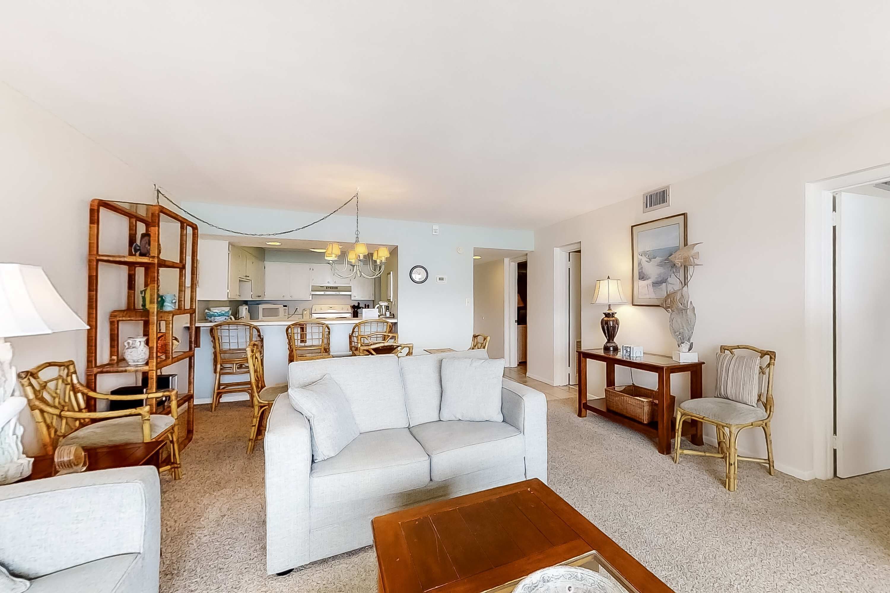 A living room with a sofa, chairs, a coffee table, and a kitchen in the background.