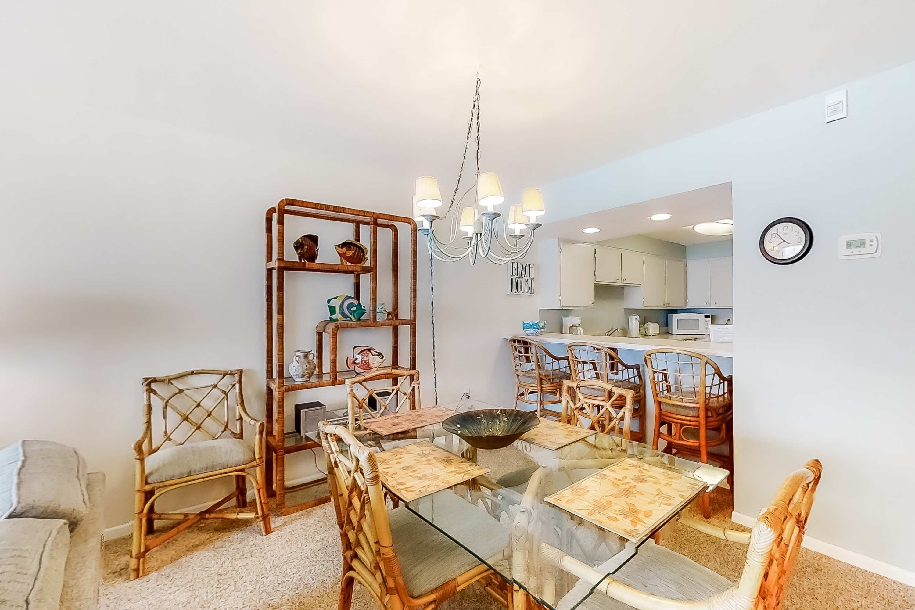 A dining area with a glass table, wicker chairs, and a chandelier.