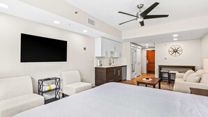 A modern hotel room with a large bed, two sofas, a TV, a ceiling fan, a kitchen area, and a dining table. - Upscale studio at The Village of Baytowne Wharf with AC, pool, hot tub & gym (Miramar Beach)