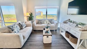 Una sala de estar moderna con sofá, mesa de centro y televisor, con un amplio ventanal con vista a la ciudad.