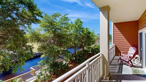 A balcony with a view of a swimming pool and trees, a wooden chair, and a small table. - Waterfront Home Close to Beach w/ Shared Pool, Hot Tub, Free WiFi, & Central AC (Mexico Beach)