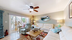 Ein Wohnzimmer mit Deckenventilator, einer Fischskulptur auf einem Couchtisch, einem weißen Sofa und einem gemusterten Teppich.