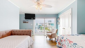Ein Schlafzimmer mit zwei Betten, einem Deckenventilator, einem Fernseher und einem Balkon mit Blick auf Gebäude.