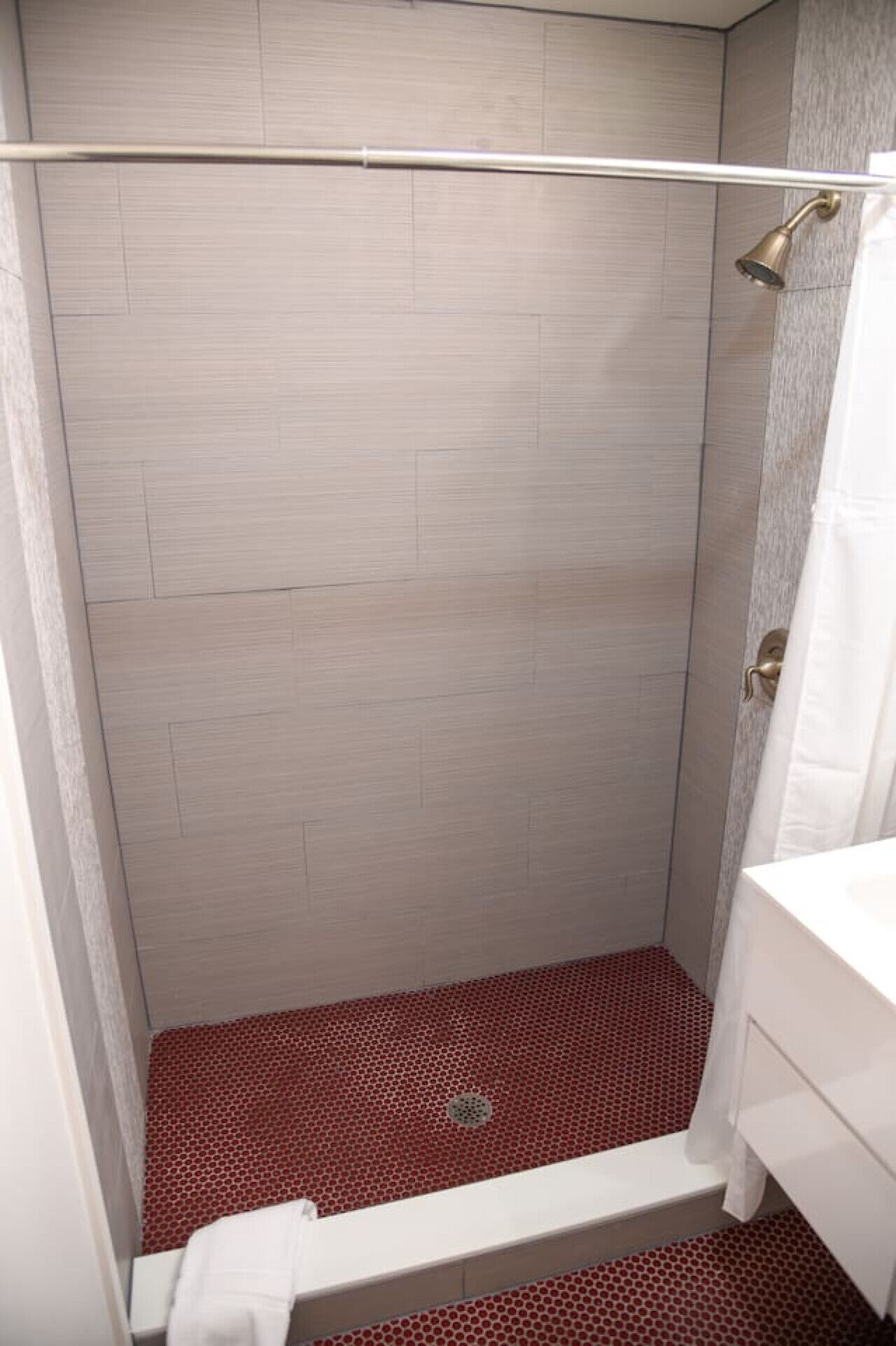 A shower with a metal rod, a white towel, and a red patterned floor.