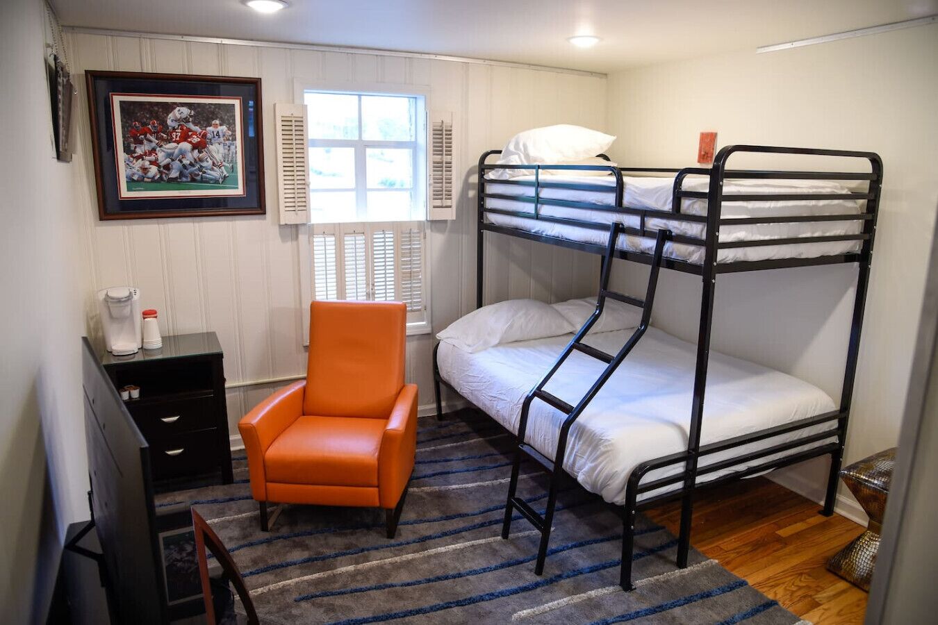 A bunk bed room with a chair, a small table with a coffee maker, and a framed sports picture on the wall.