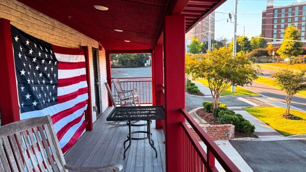 Un espace extérieur abrité, doté d’une rambarde rouge, d’une table, de deux chaises et d’un drapeau américain.