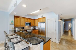 A modern kitchen with wooden cabinets, stainless steel appliances, and a granite countertop. - Floor Condo Gulf Front, Nearby Shopping & Dining Seasonal Beach Service (Fort Walton Beach)